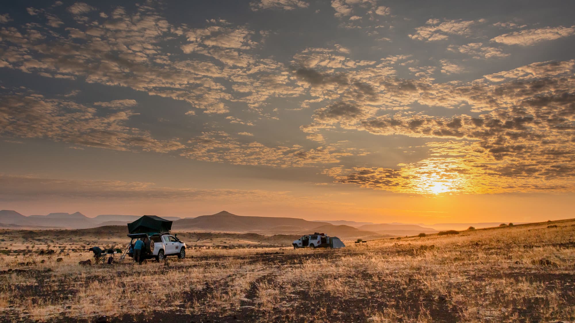 Camping bei Heins Camp in der Palmwag-Konzession: zwei Geländewagen, goldenes Abendlicht und rundherum die ungezähmte Weite des Damaralands.